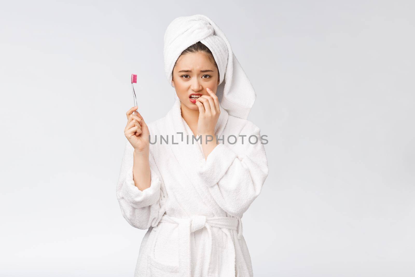 Unhappy beautiful woman brushing her teeth on white background.