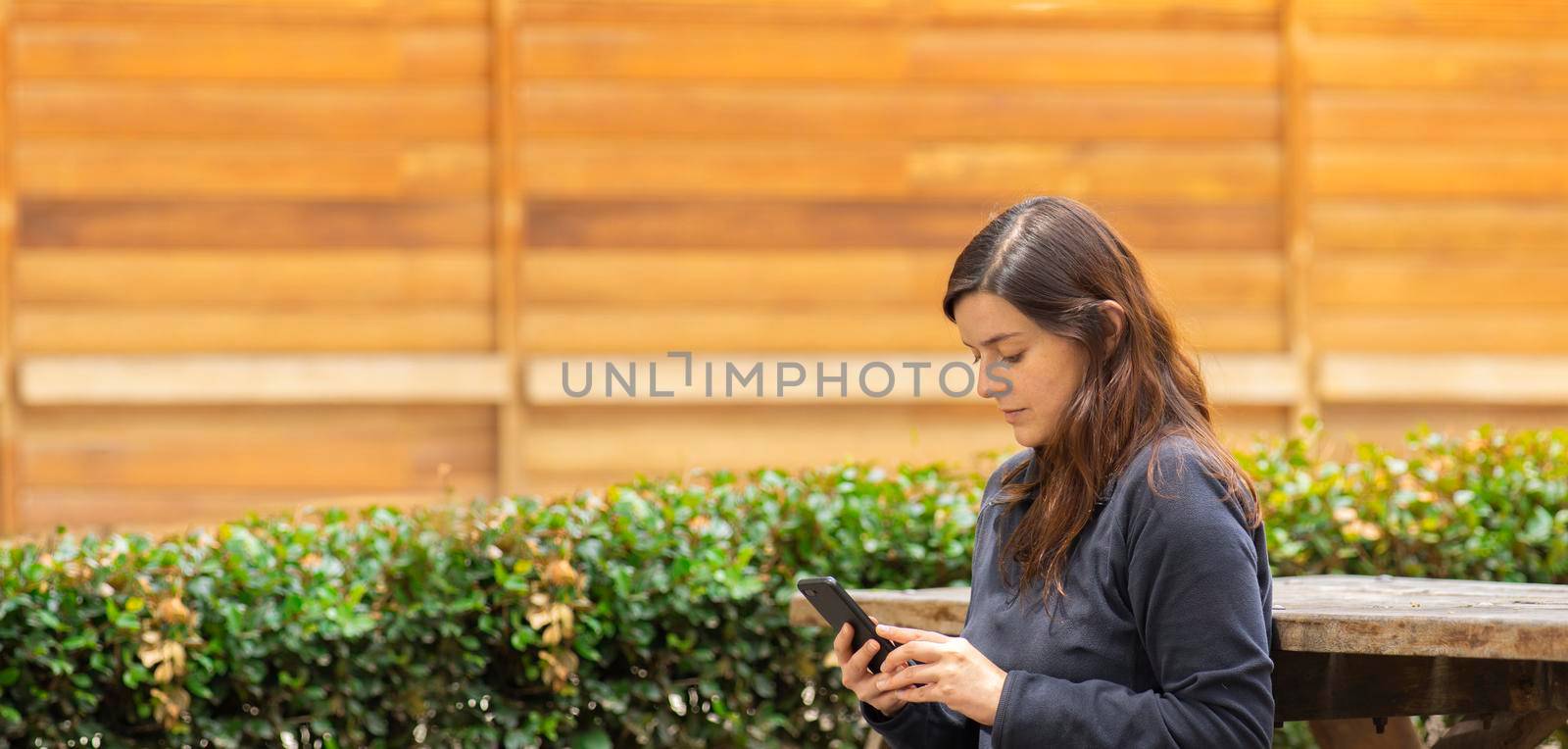 Beautiful Hispanic young woman reading a message on her cell phone sitting on a park bench by alejomiranda