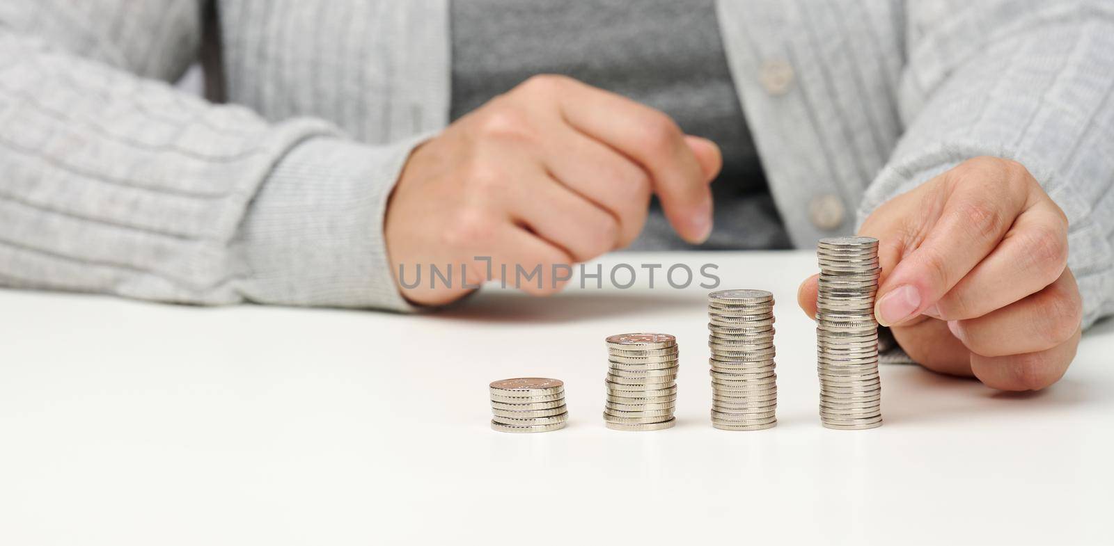 woman is sitting at the table and a stack of coins on the table. Calculation of expenses and income, subsidy, tax