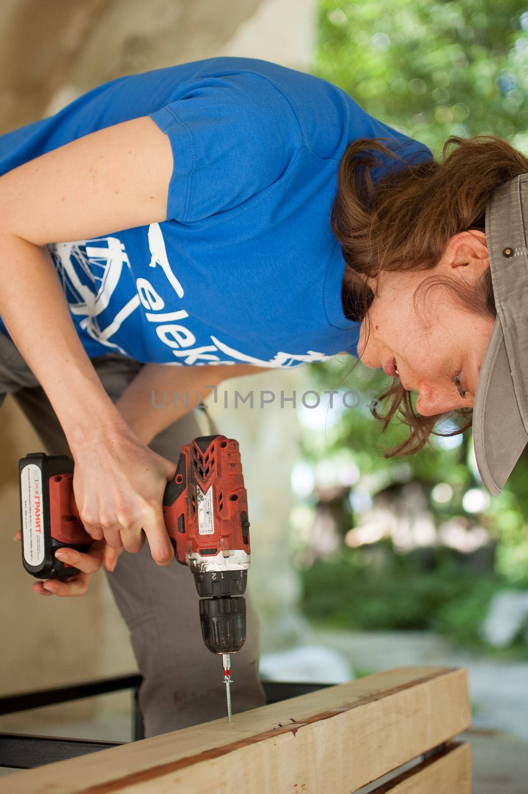 13.08.2021 - Ukraine, Goshcha, voluntary event, skilled young female worker is using power screwdriver drilling during construction wooden bench, gender equality, feminism. by balinska_lv