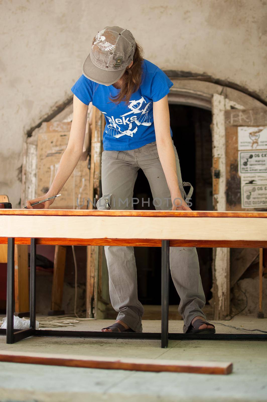 13.08.2021 - Ukraine, Goshcha, female worker are making some marks on wooden plank for future holes using pencil for assembling bench during voluntary event