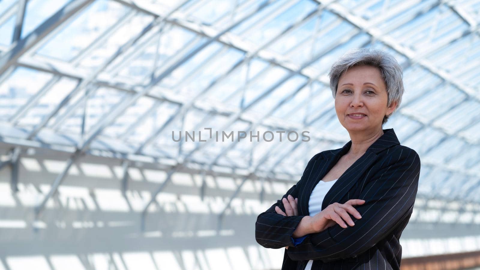 Happy successful mature Asian businesswoman posing with arms folded in the business building
