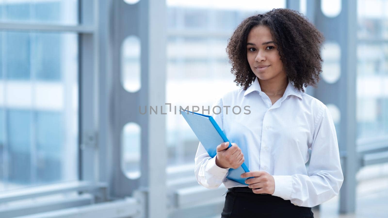 Happy african business woman holding folder of documents standing near window in office