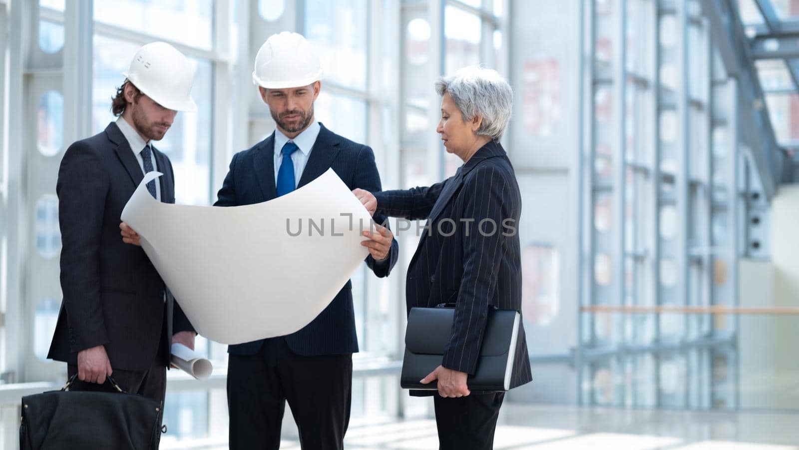 Multi ethnic business architect people in safety helmets discussing blueprint standing in the lobby at office