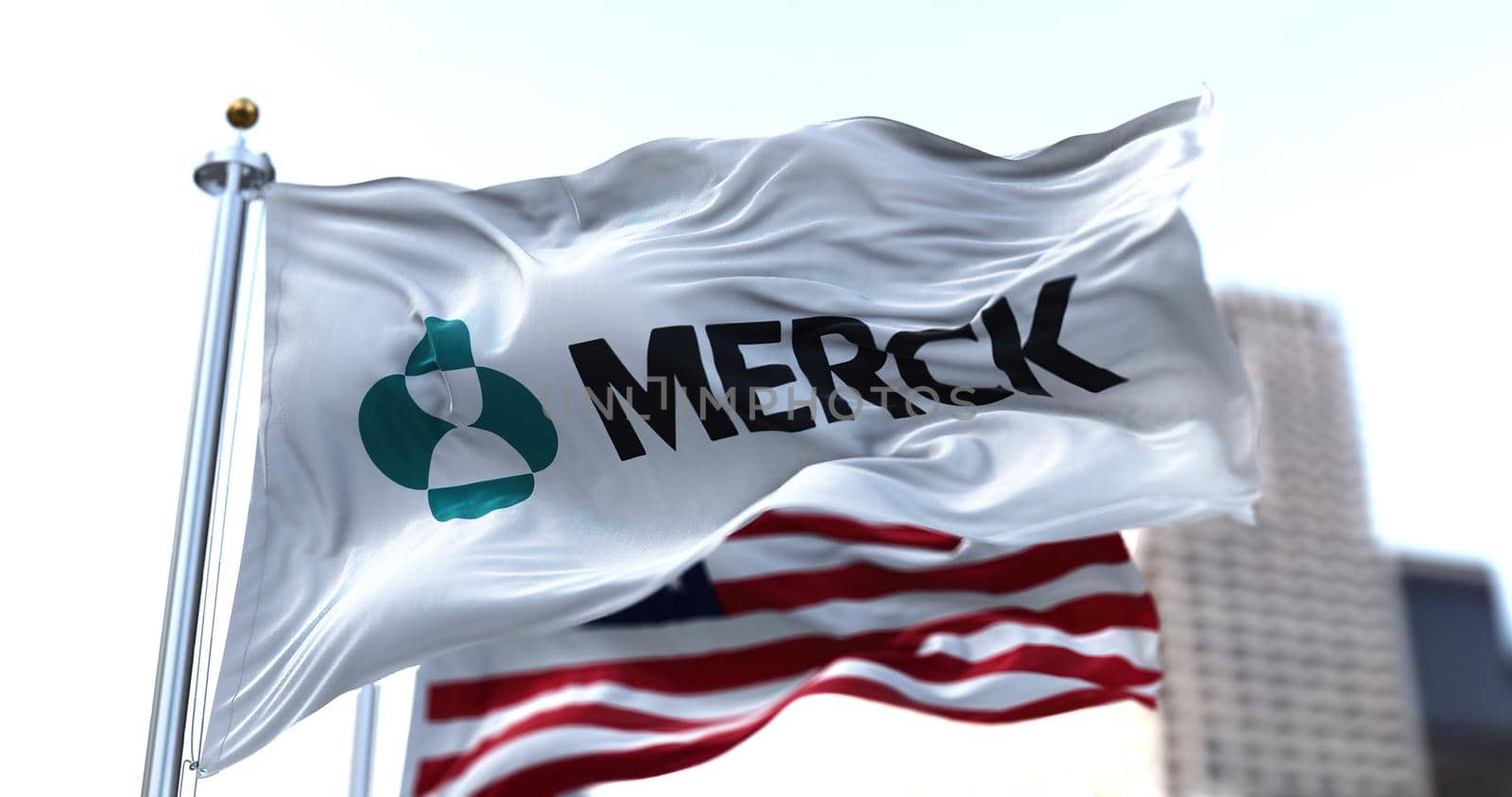 New York ,USA, October 2021: the flag with the logo of Merck waving in the wind with the American flag blurred in the background. Merck is an American multinational pharmaceutical company