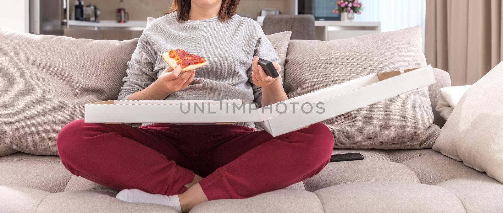 Girl eating pizza sitting on couch and watching tv