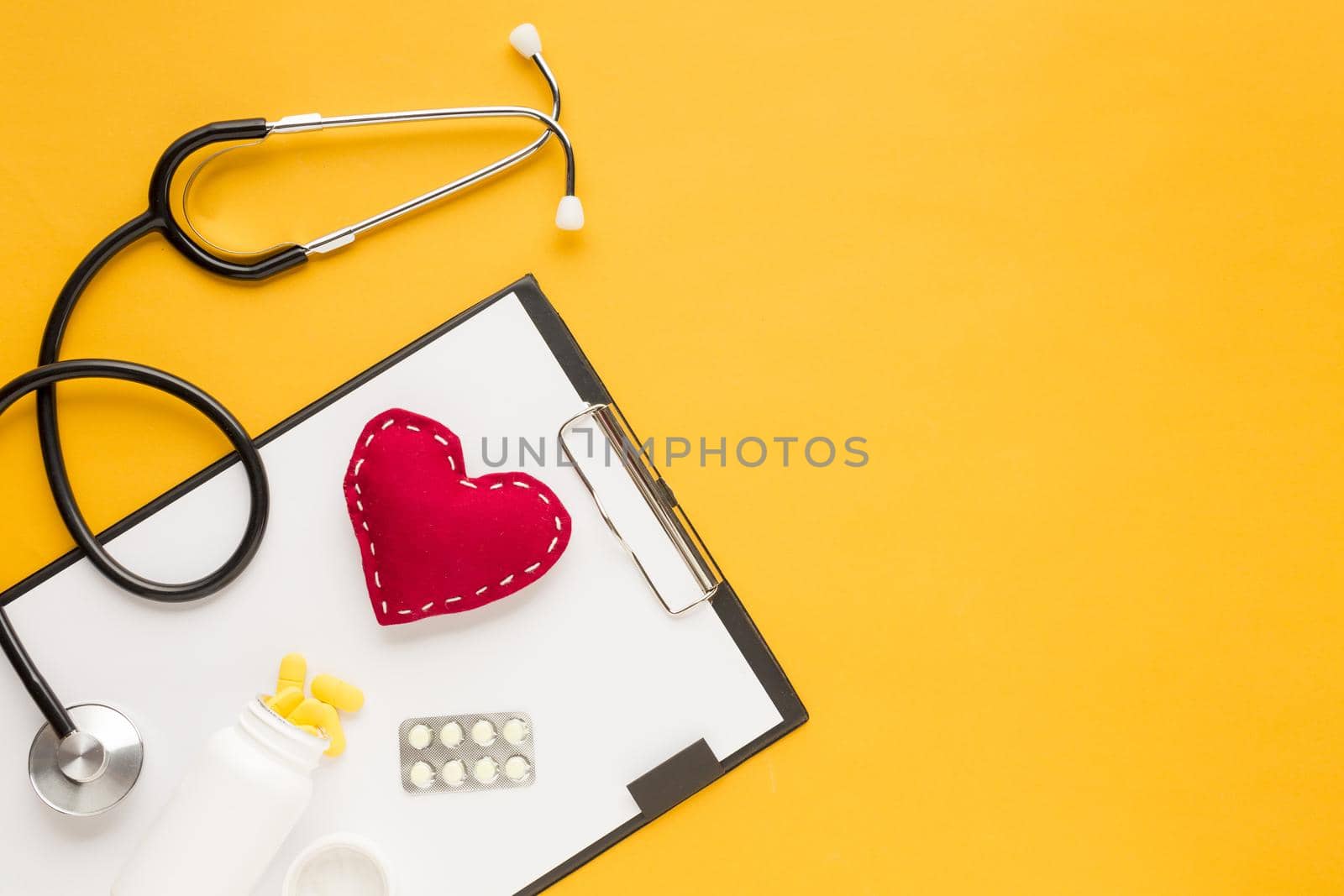 stethoscope stitched heart medicine falling from bottles blister packed medicine with clipboard yellow table. High quality beautiful photo concept by Zahard