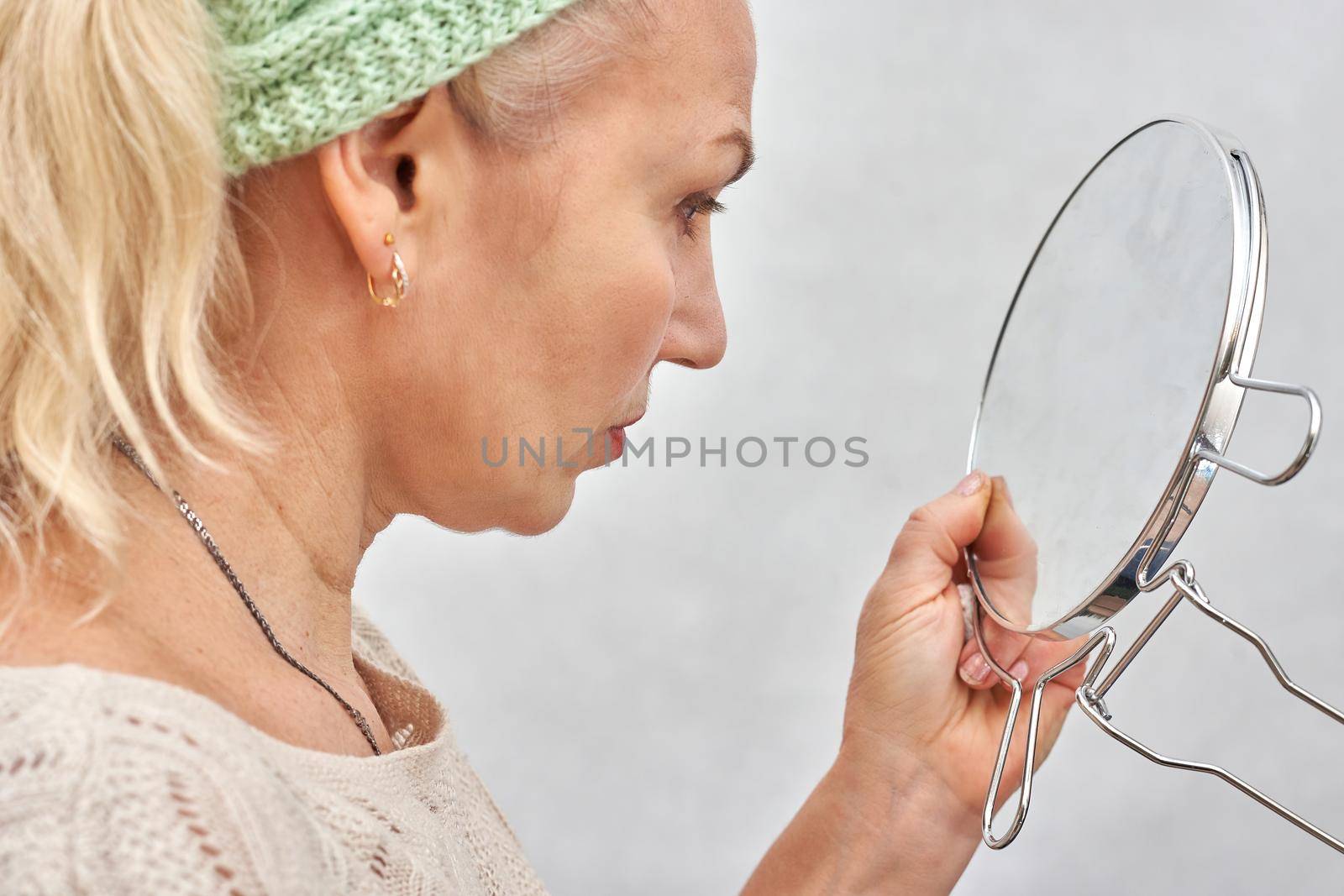 A woman aged looks in the mirror before applying makeup. Woman in beauty parlor on white background