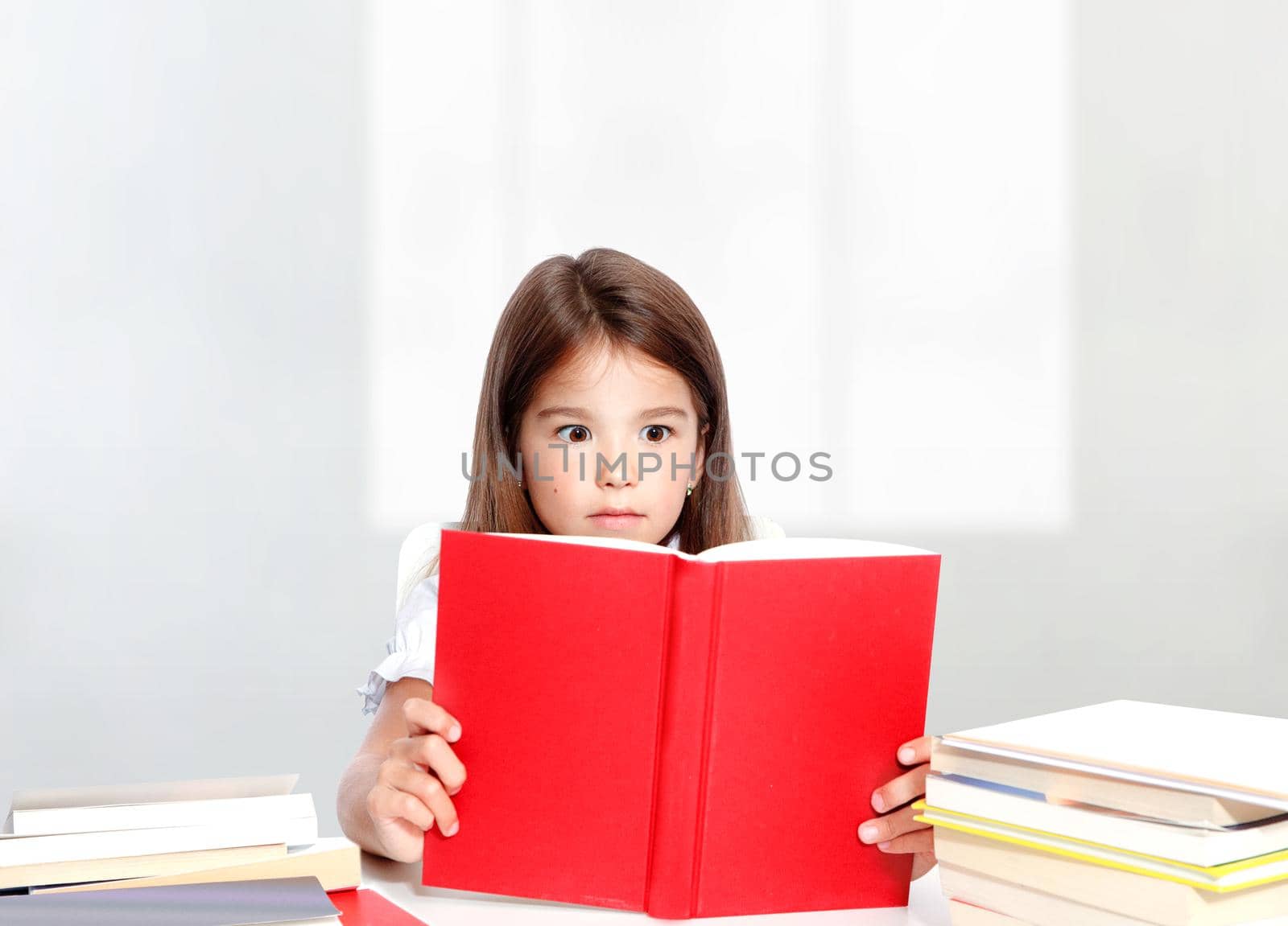 Young cute girl sitting at the table and reading a book by Taut