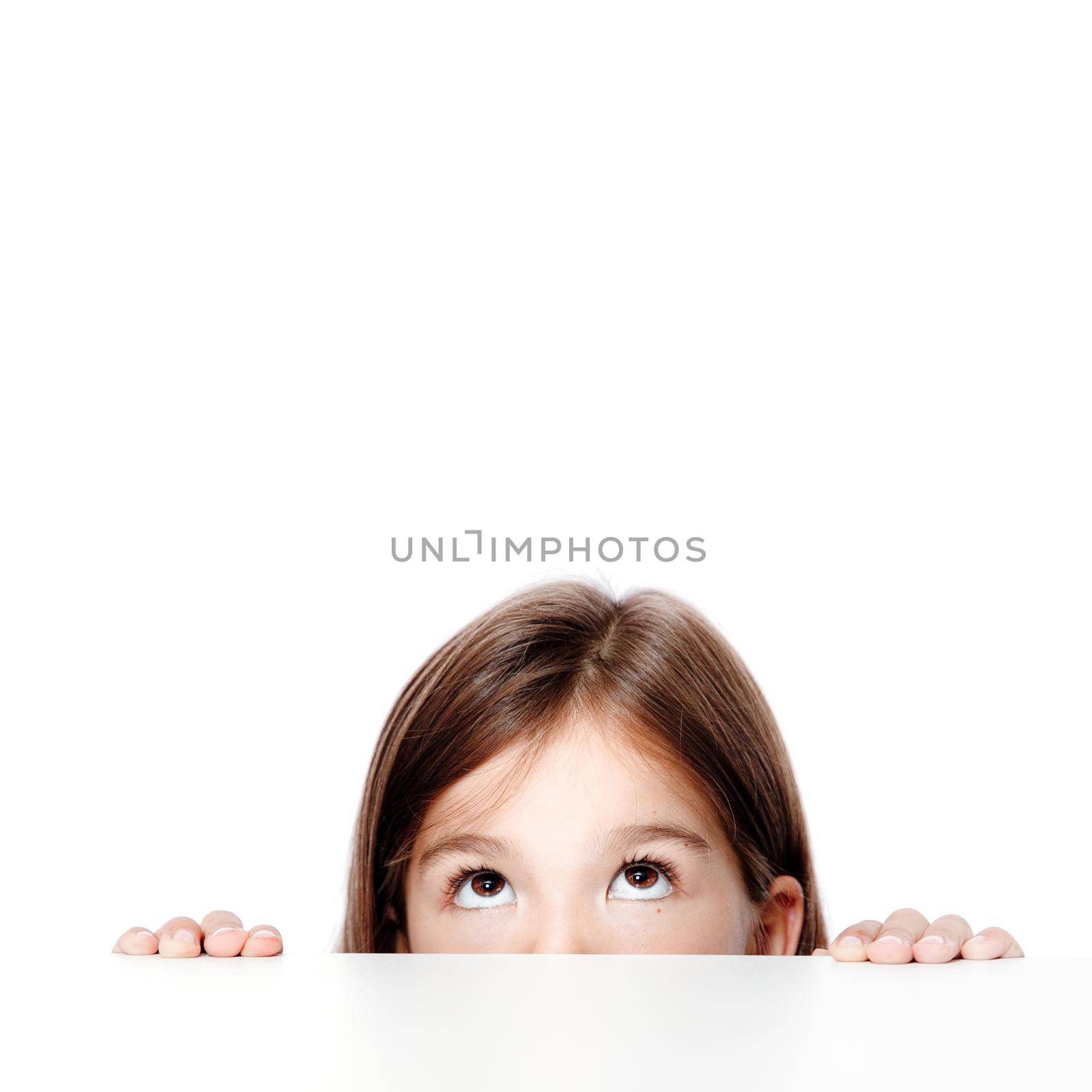 Cute little child girl looking up on the desk at school. by Taut