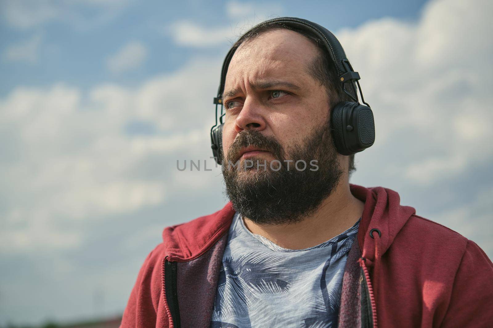 Middle-aged European man in headphones outdoors listening to music against the background of the sky