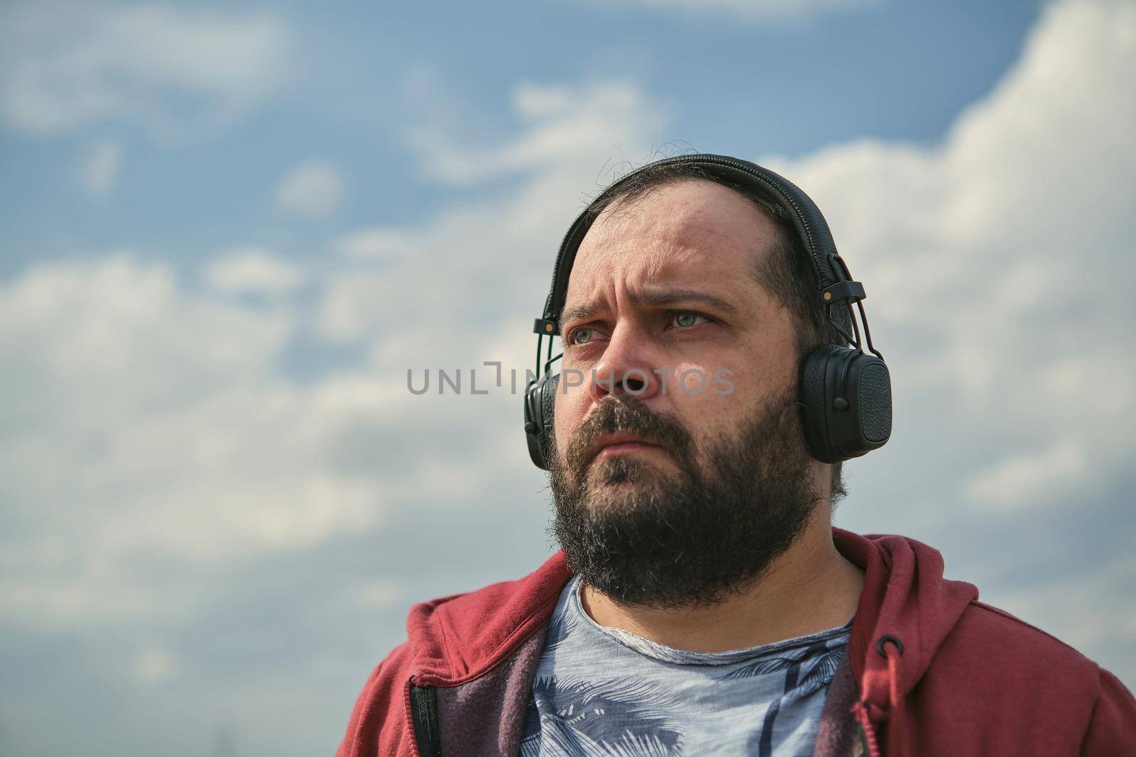 Middle-aged European man in headphones outdoors listening to music against the background of the sky