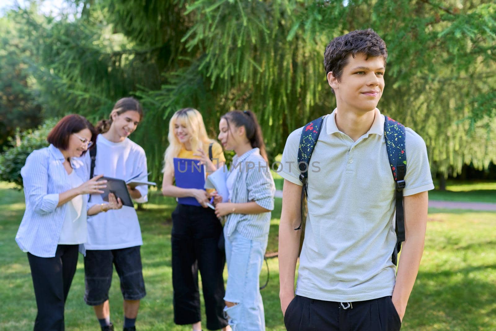 Portrait of male student in park campus, group of teenagers with teacher background. Adolescence, college, high school, education concept.