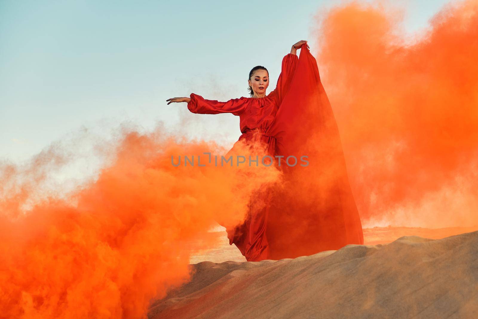 Woman in red dress dancing in the desert at blue sky