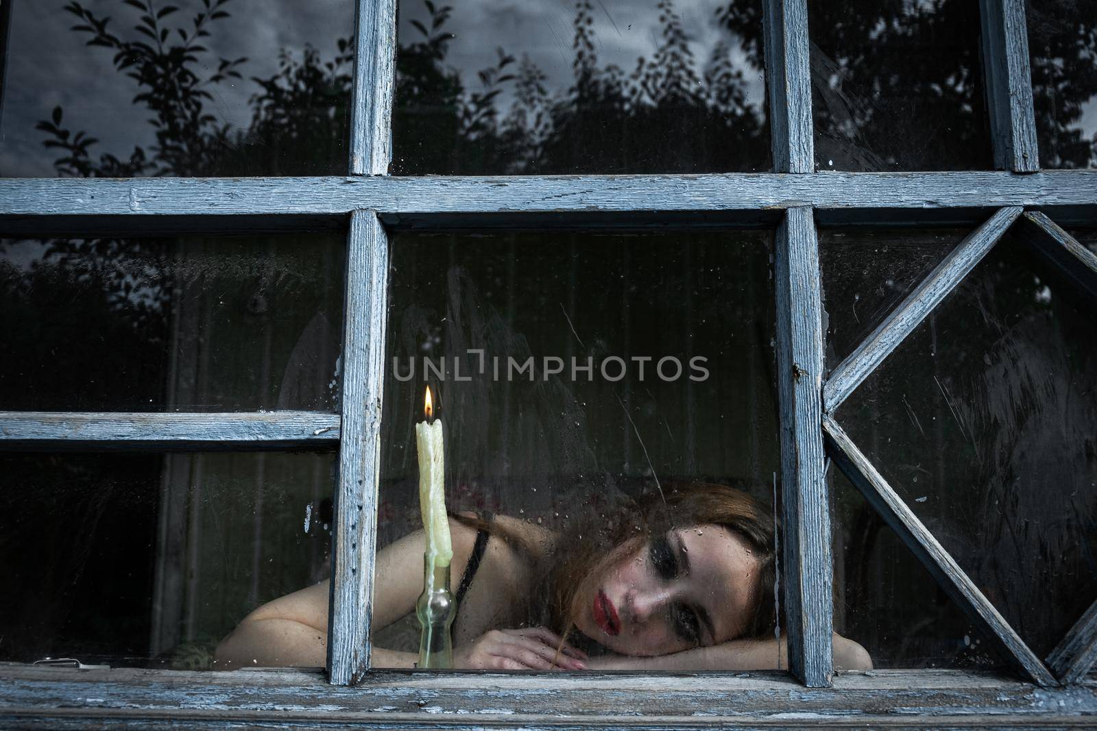 Beautiful sad young girl looking out the window with a candle by snep_photo