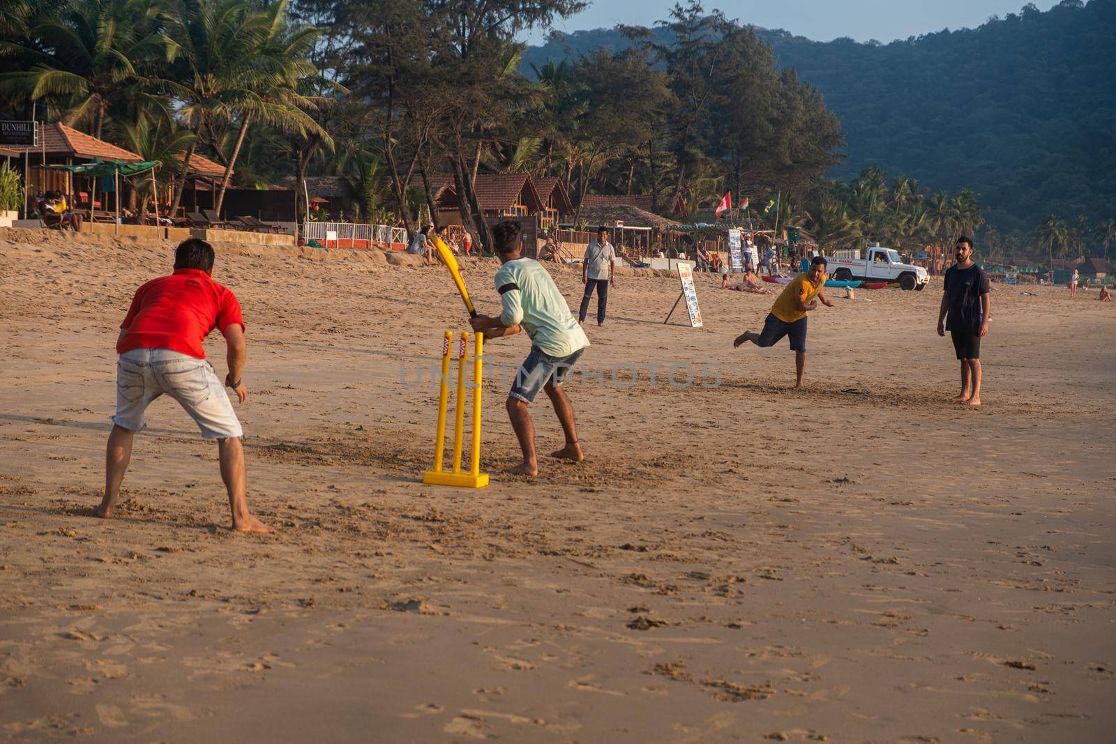 Group of Indian adults playing cricket on beach at sunset, Goa, India