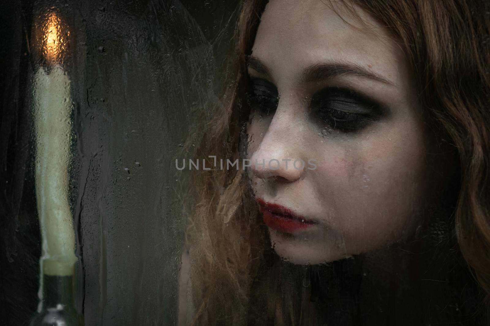 Beautiful sad young girl looking out the window with a candle, good for book cover