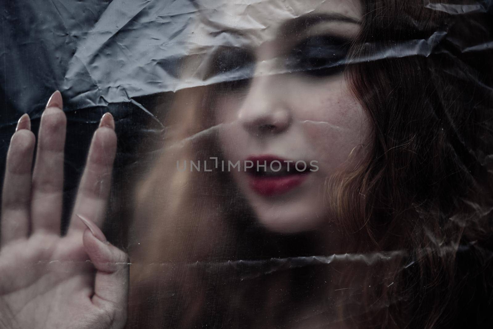Young beauty sad woman trapped behind a plastic sheet as protection against COVID-19. Nicely fits for book cover by snep_photo
