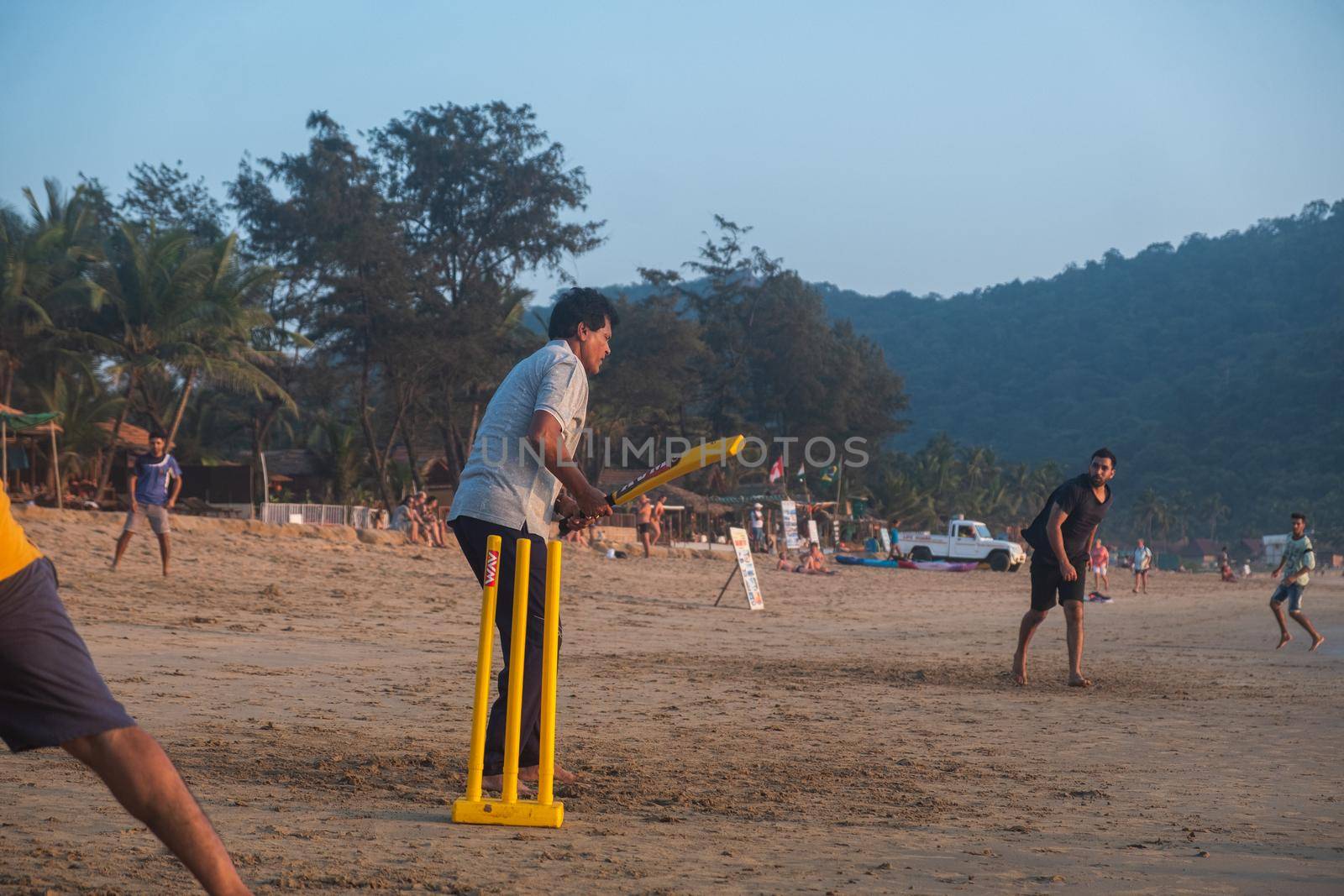 Group of Indian adults playing cricket on beach at sunset, Goa, India