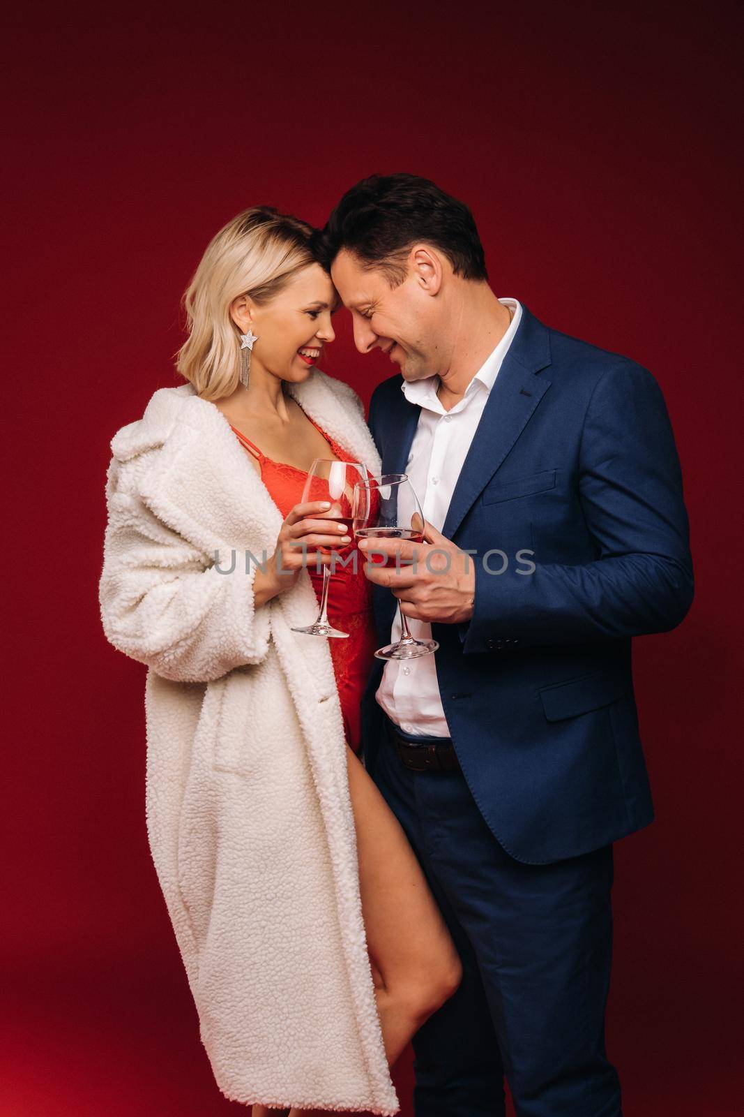 A man and a woman in love with a glass of champagne on a red background embrace.