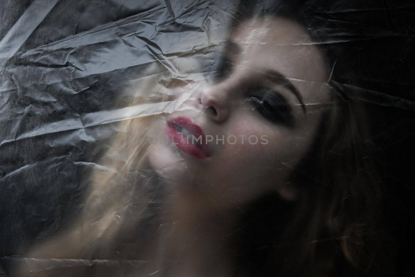 Young beauty sad woman trapped behind a plastic sheet as protection against COVID-19. Nicely fits for book cover by snep_photo