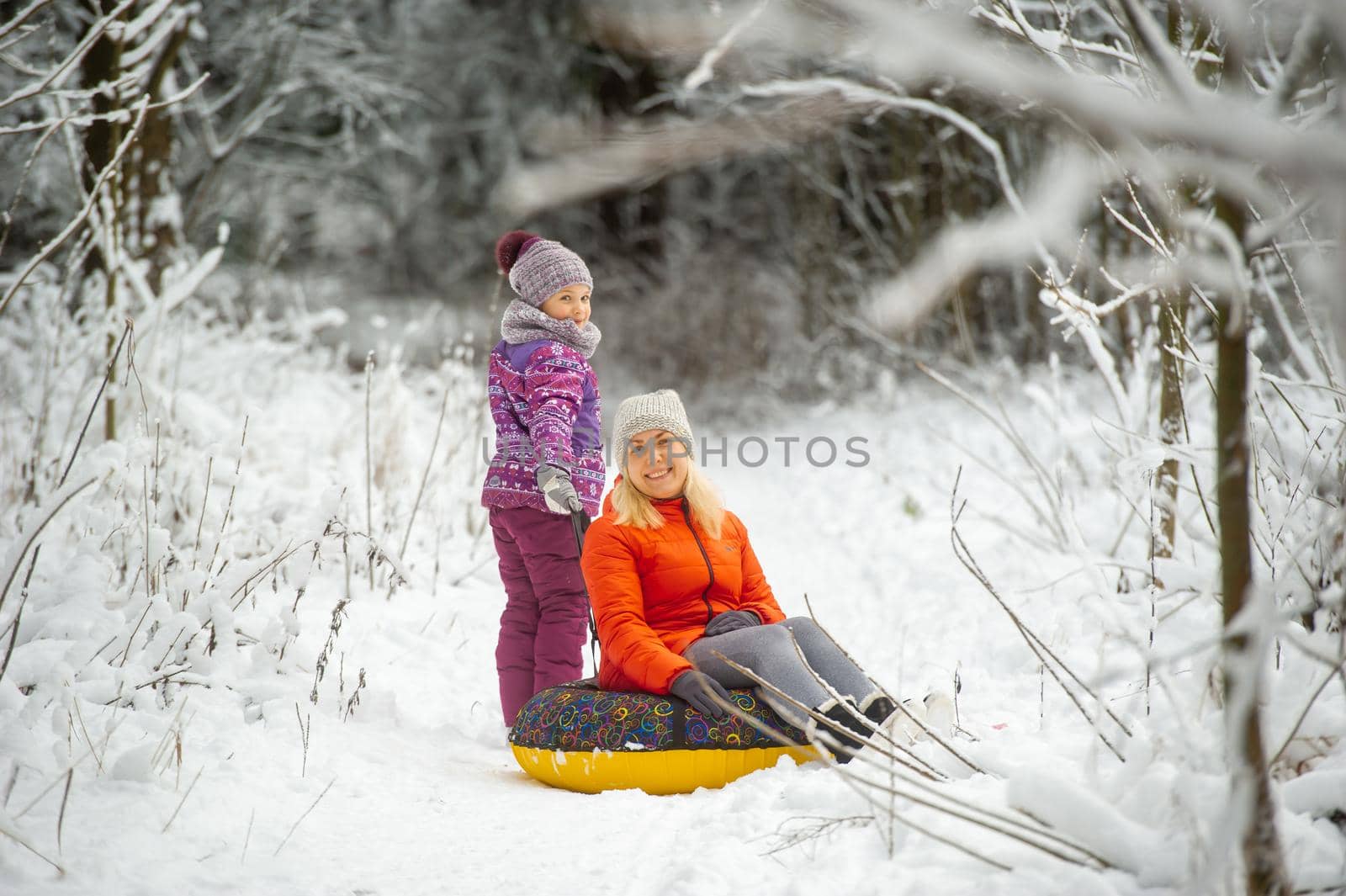 Family mom and daughter in winter with an inflatable circle walk through the snow-covered forest by Lobachad