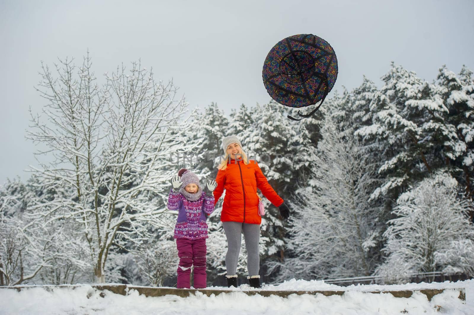 Family mom and daughter in winter with an inflatable circle walk through the snow-covered forest.