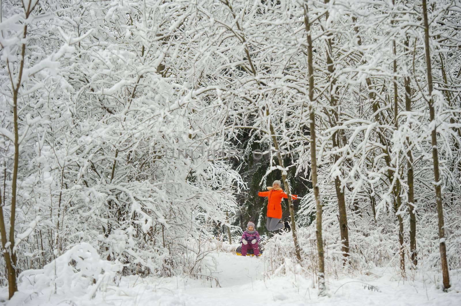 Family mom and daughter in winter with an inflatable circle walk through the snow-covered forest by Lobachad