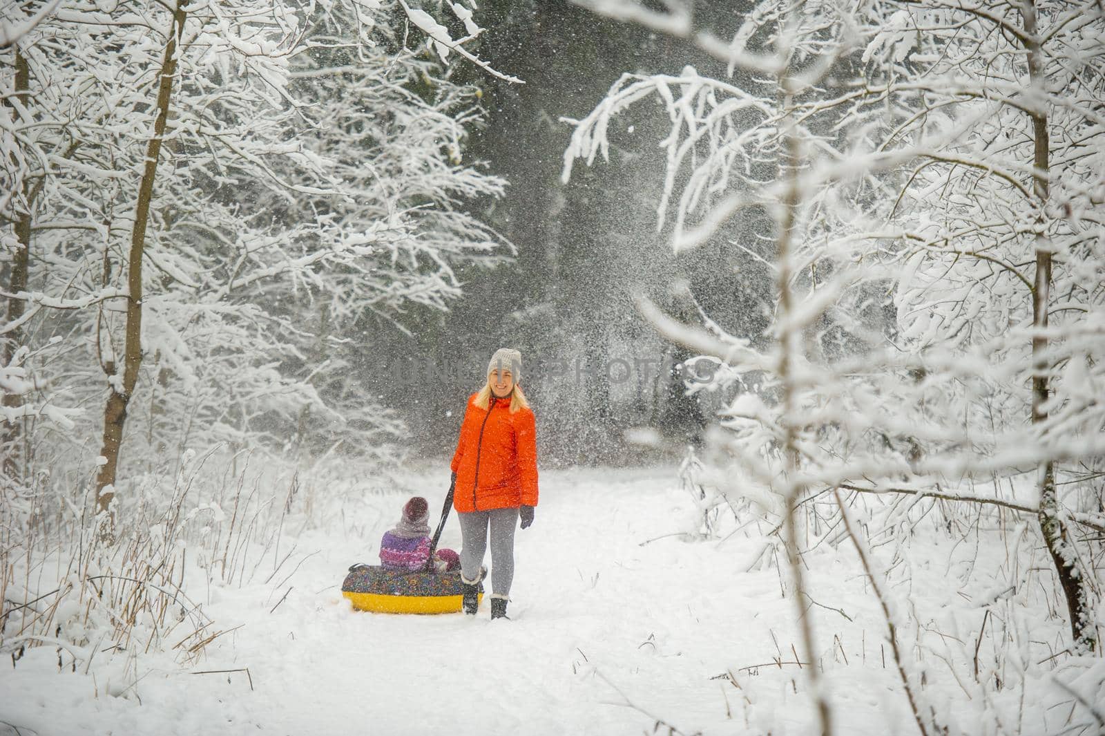 Family mom and daughter in winter with an inflatable circle walk through the snow-covered forest by Lobachad