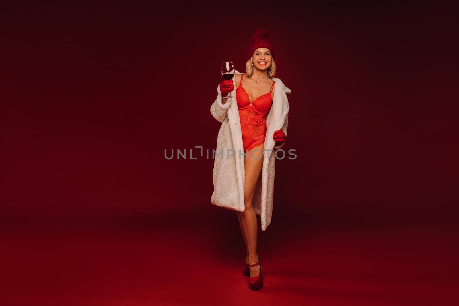 portrait of a smiling girl in a white fur coat and underwear holding a glass of champagne on a red background by Lobachad