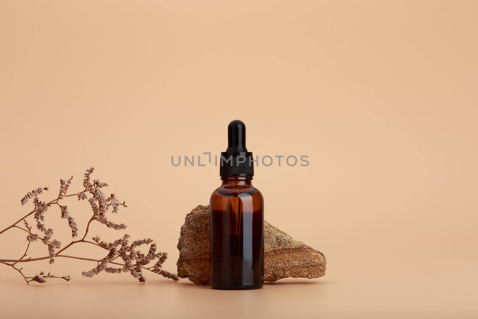 Skin serum bottle next to natural stone and dry flower against beige background with copy space by Senorina_Irina