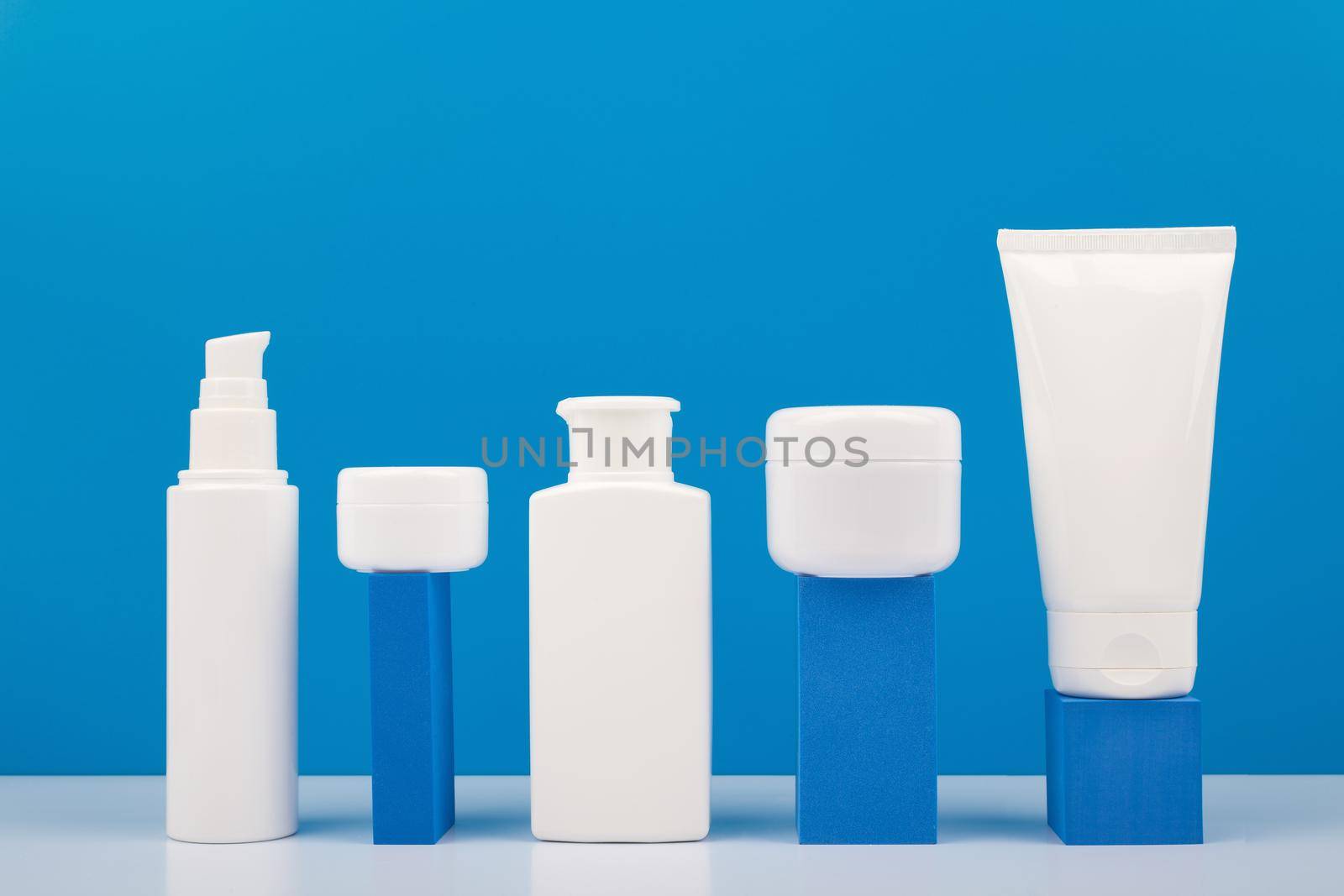 Set of cosmetic products for daily skincare on white table and geometric props against bright blue background by Senorina_Irina