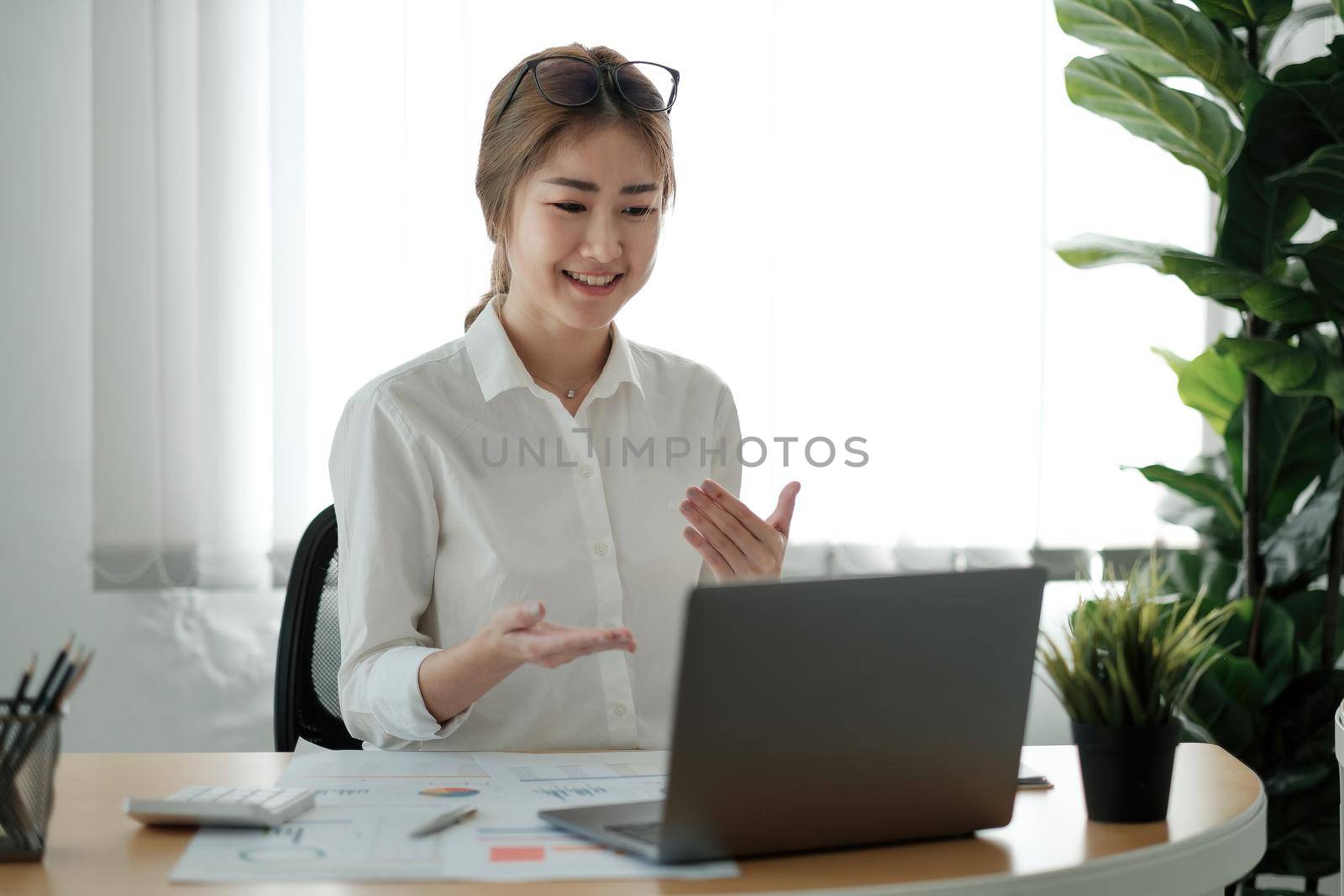 Smiling young female employee at home speak talk on video call on laptop with diverse colleagues. Asian woman worker have webcam conference or digital web team meeting or briefing with coworkers by nateemee