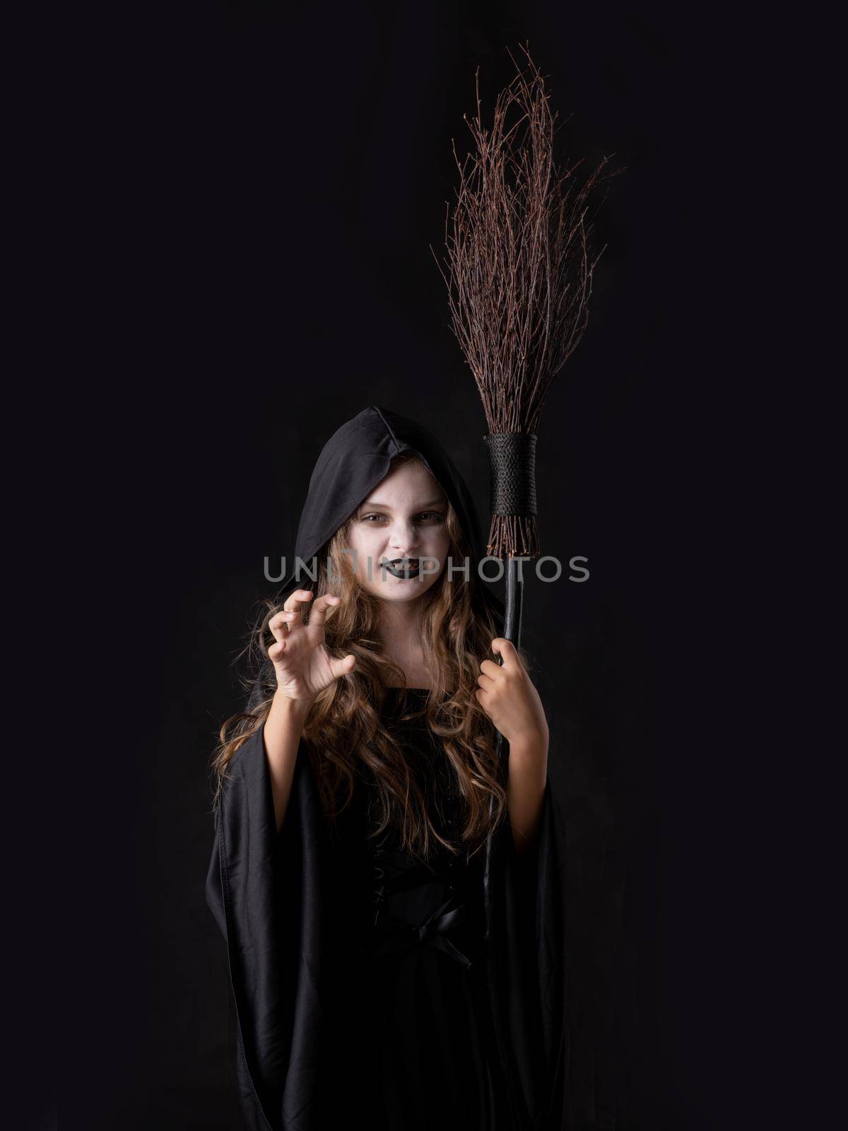 Girl in halloween evil angry witch costume grin snarl hold broom isolated on black background