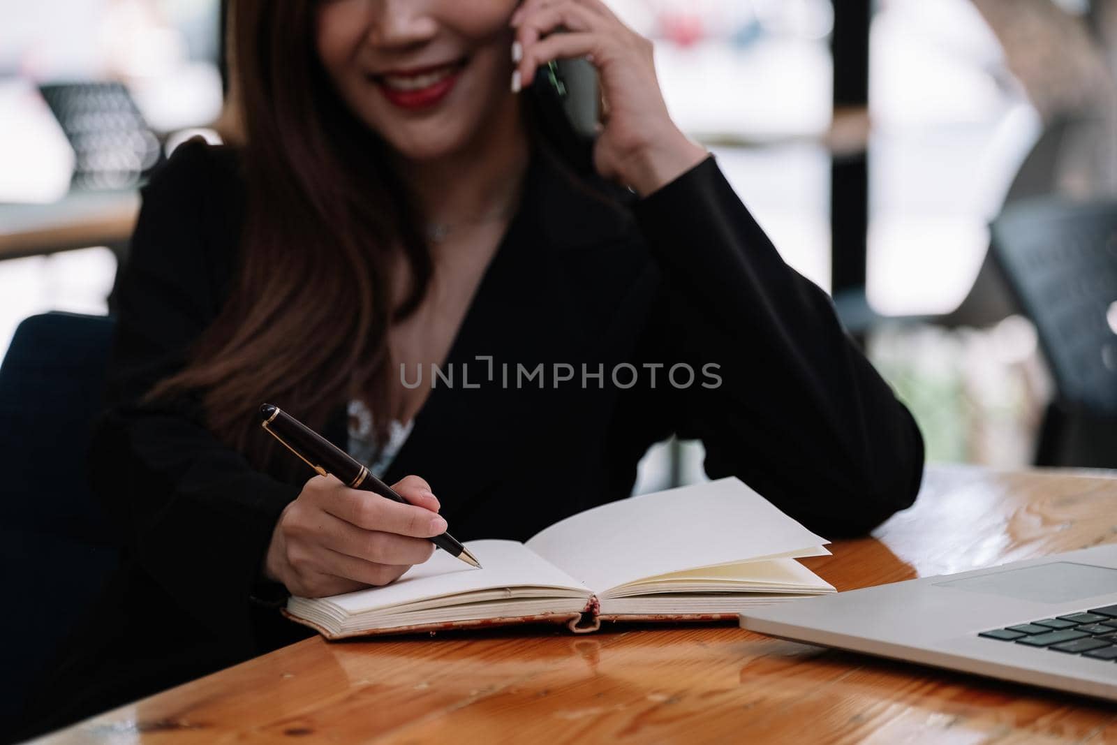 Closeup image of a woman writing and taking note on notebook during call mobile phone in office. by nateemee