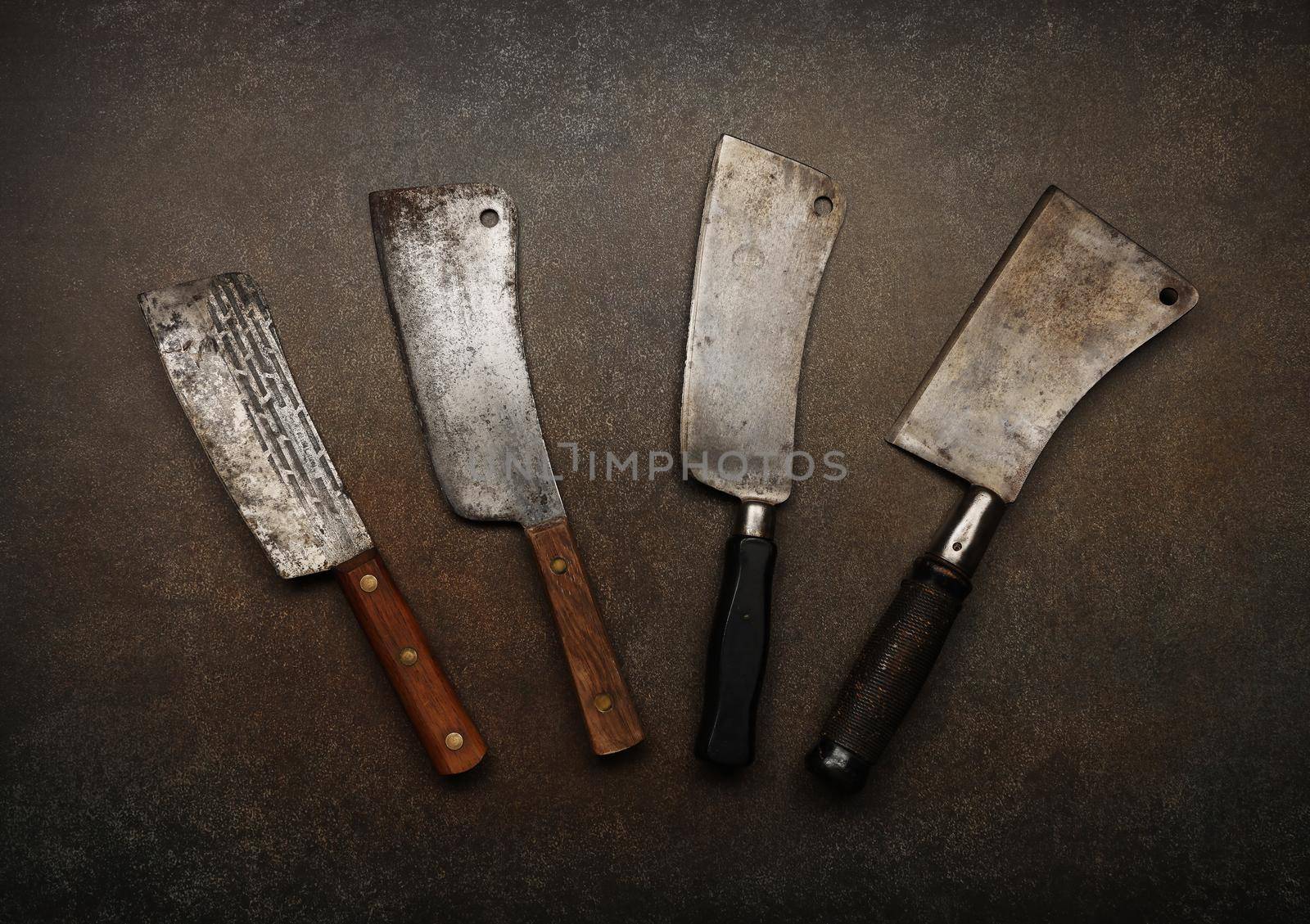 Close up vintage butcher meat cleavers on cutting board or grunge brown stone table surface with copy space, elevated top view, directly above