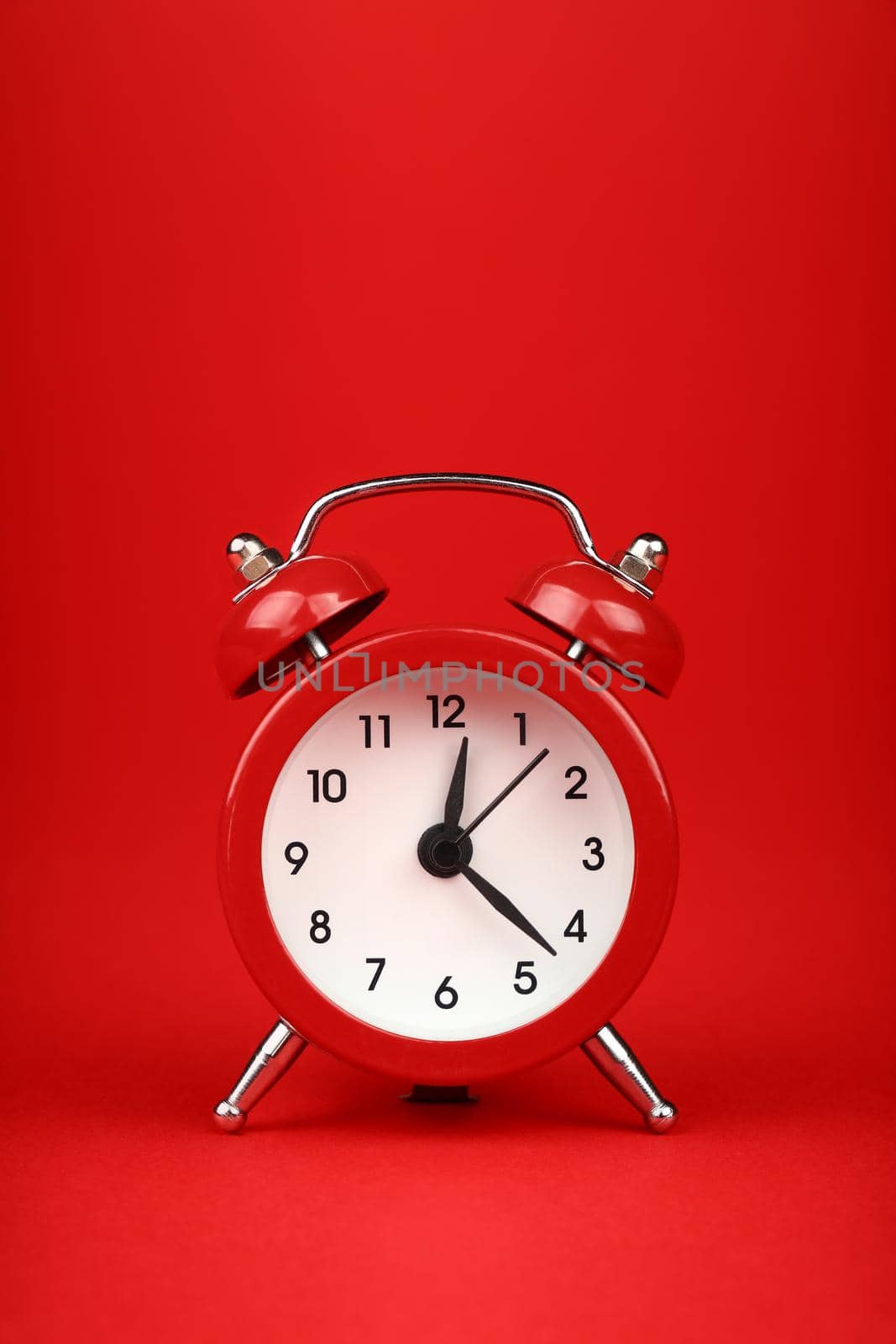 Close up one small red metal twin bell retro alarm clock over red paper background with copy space, low angle front view