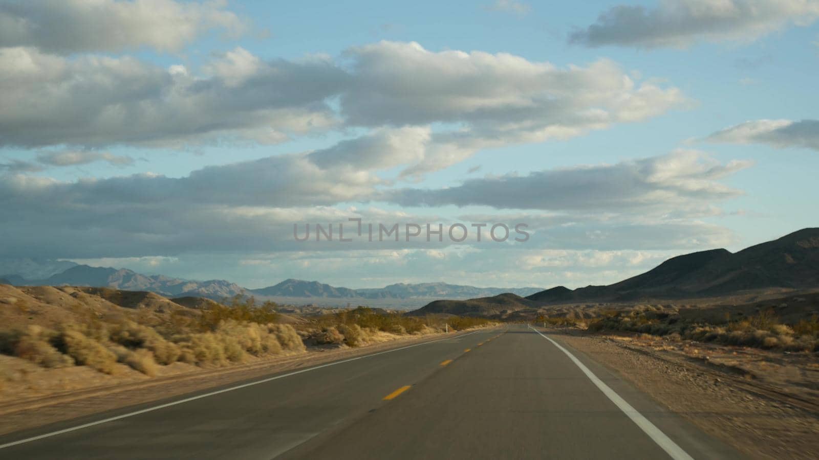 Road trip, driving auto from Death Valley to Las Vegas, Nevada USA. Hitchhiking traveling in America. Highway journey, dramatic atmosphere, sunset mountain and Mojave desert wilderness. View from car by DogoraSun