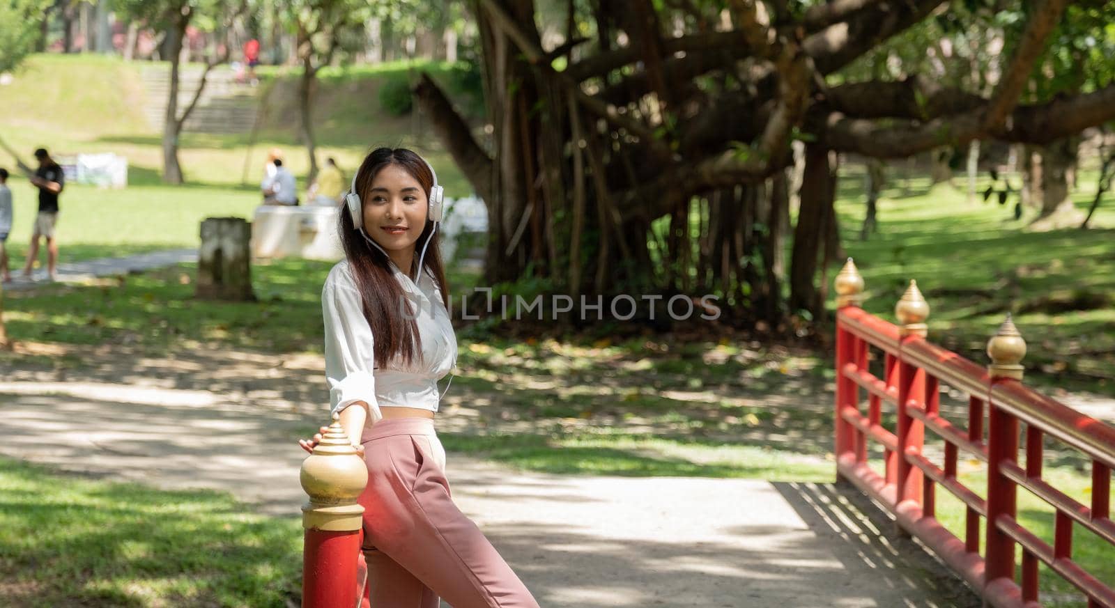 Portrait Asian Student Girl Wearing Headphones, Standing On Lawn In Park by nateemee