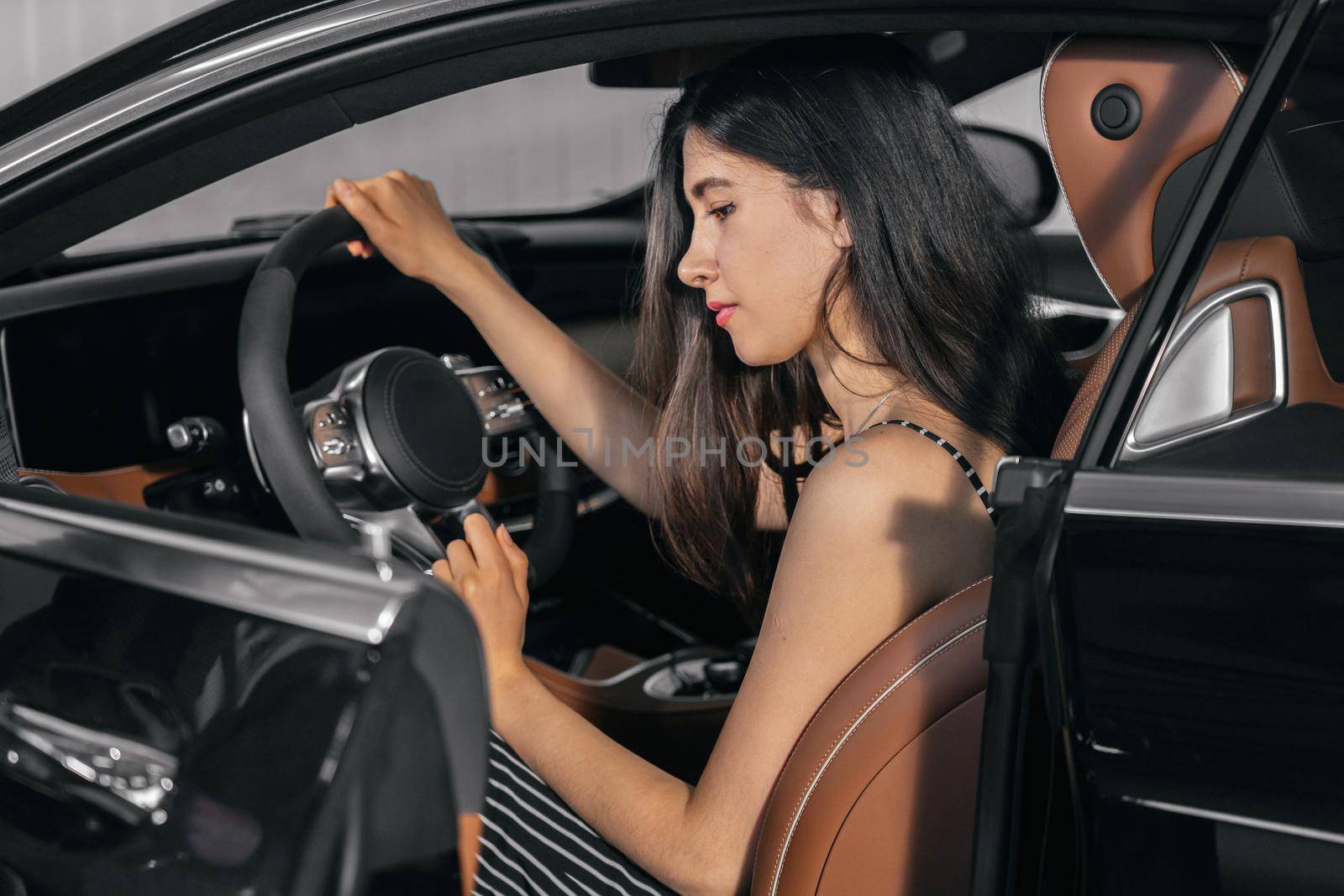 Young asian woman sitting in luxury car in garage before starting engine and driving