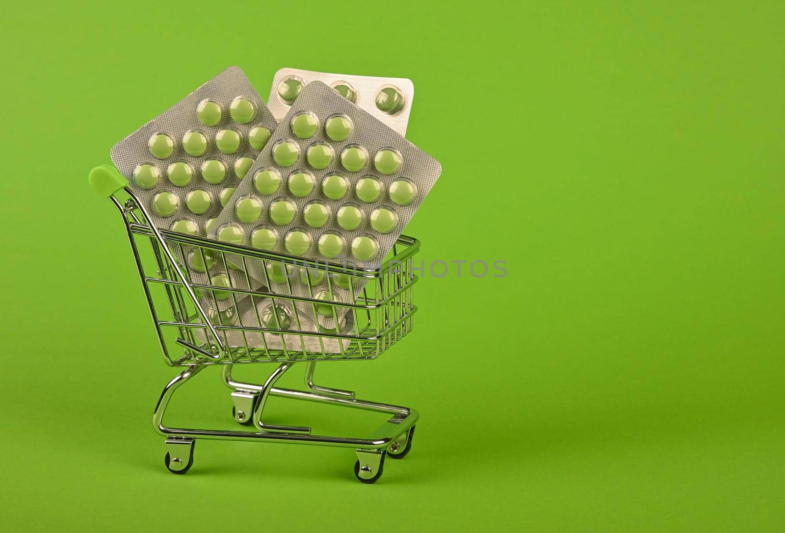 Close up several different blister packs of pills in small shopping cart over green background, concept of online medicine order delivery, low angle view