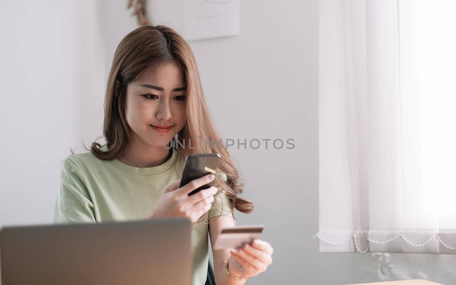 Cropped image of smiling millennial woman holding smartphone and banking credit card, involved in online mobile shopping at home, happy female shopper purchasing goods or services in internet store by nateemee