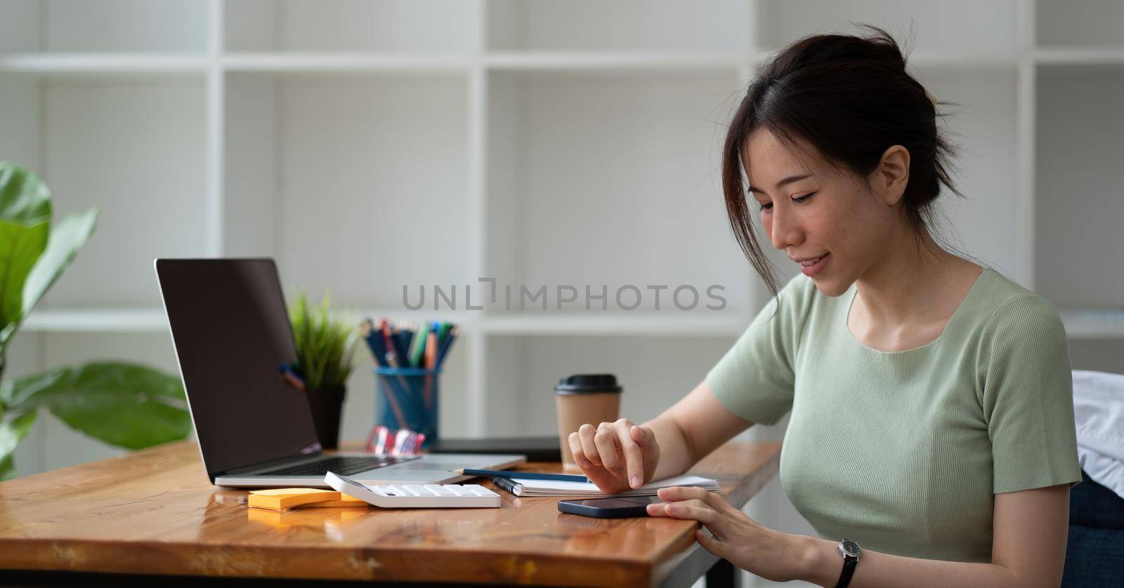 Close up hand of happy asian woman using mobile phone on working desk, business accounting concept.