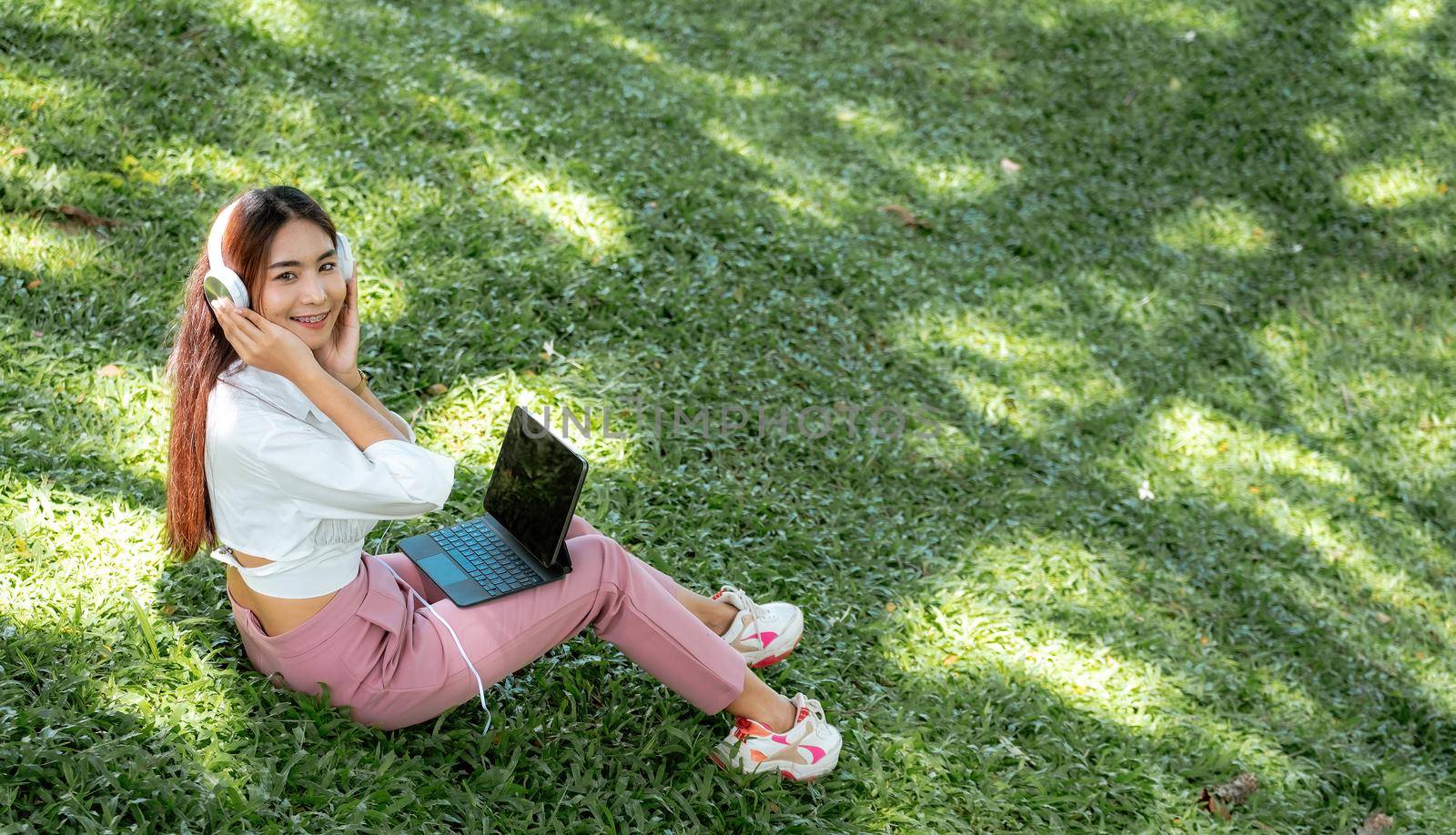 Happy student e learning with headphones and tablet at the park in a campus.