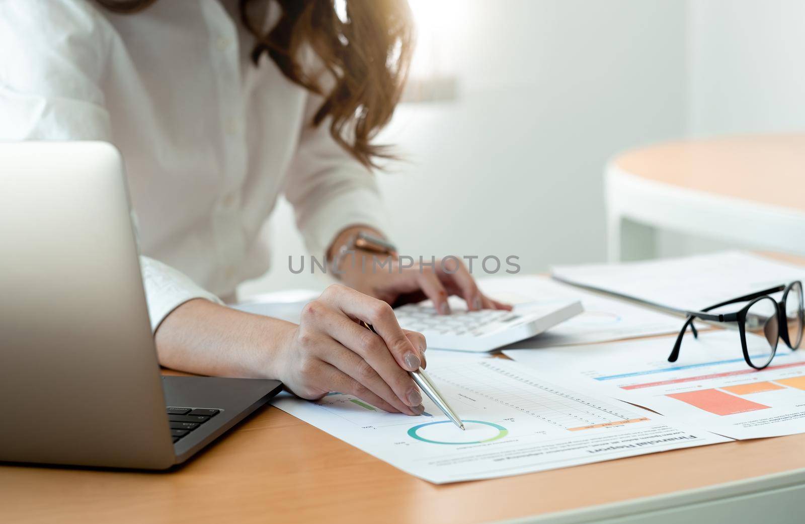 Close up of businesswoman or accountant hand holding pen working on calculator to calculate business data, accountancy document and laptop computer at office, business concept. by nateemee