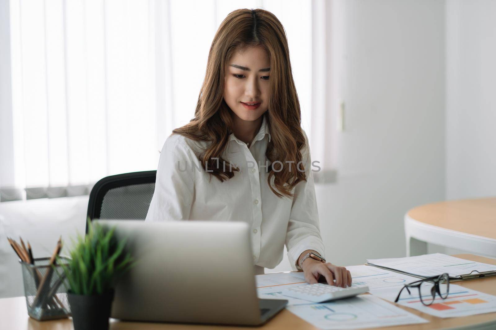 Business asian woman using calculator at working with financial report. she working with laptop computer.