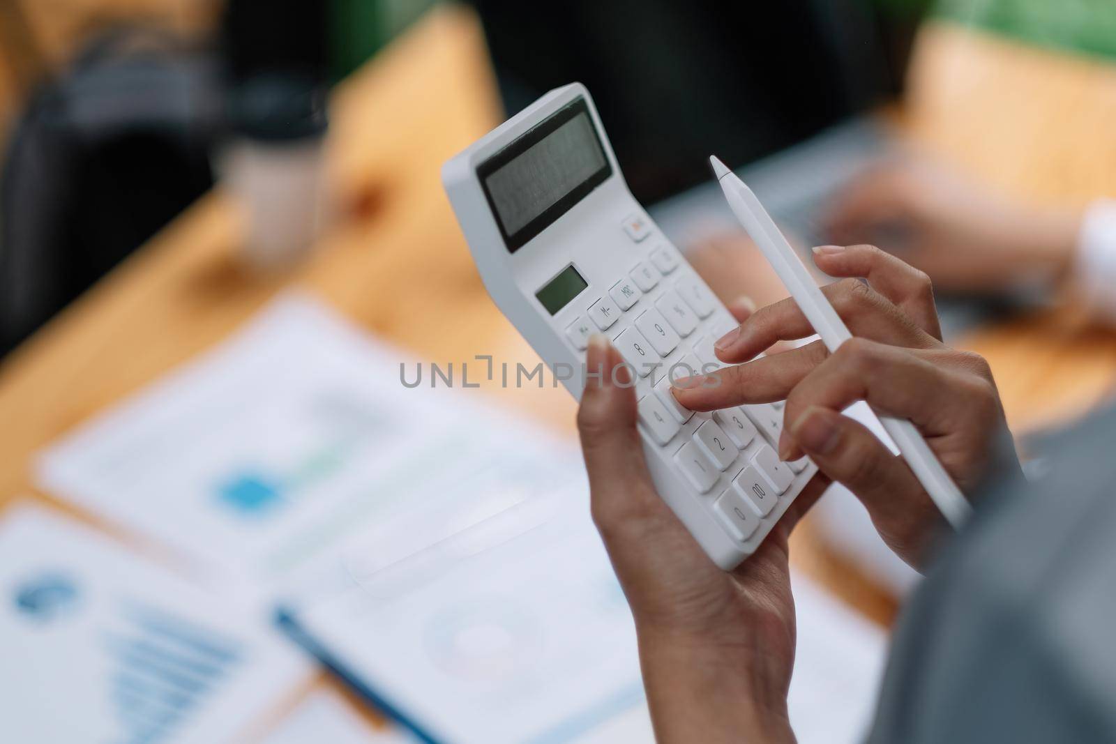 Woman entrepreneur using a calculator with a pen in her hand, calculating financial expense with working desk background by nateemee