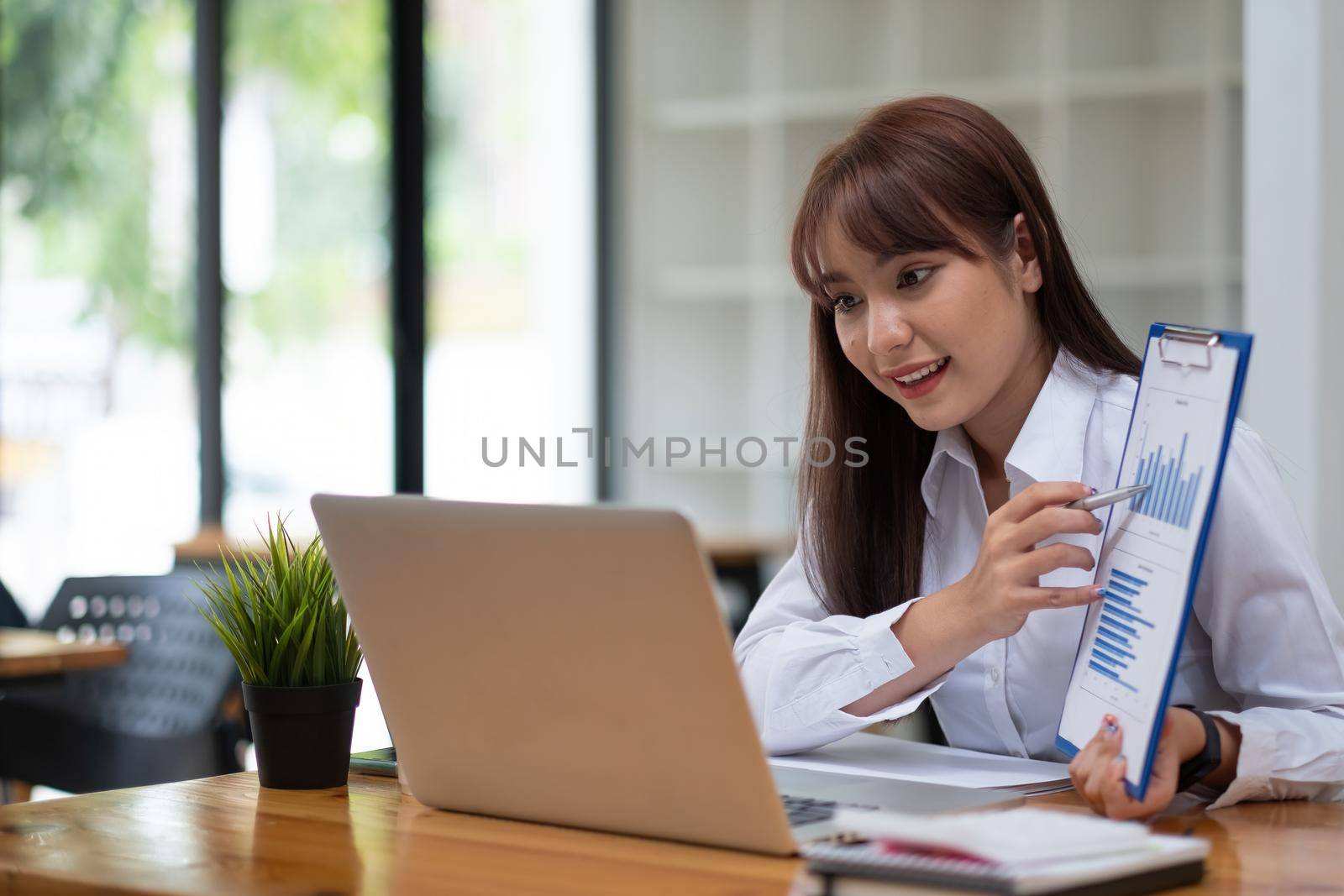 Portrait of attractive business female showing customer engagement graph report on online meeting via laptop at office by nateemee