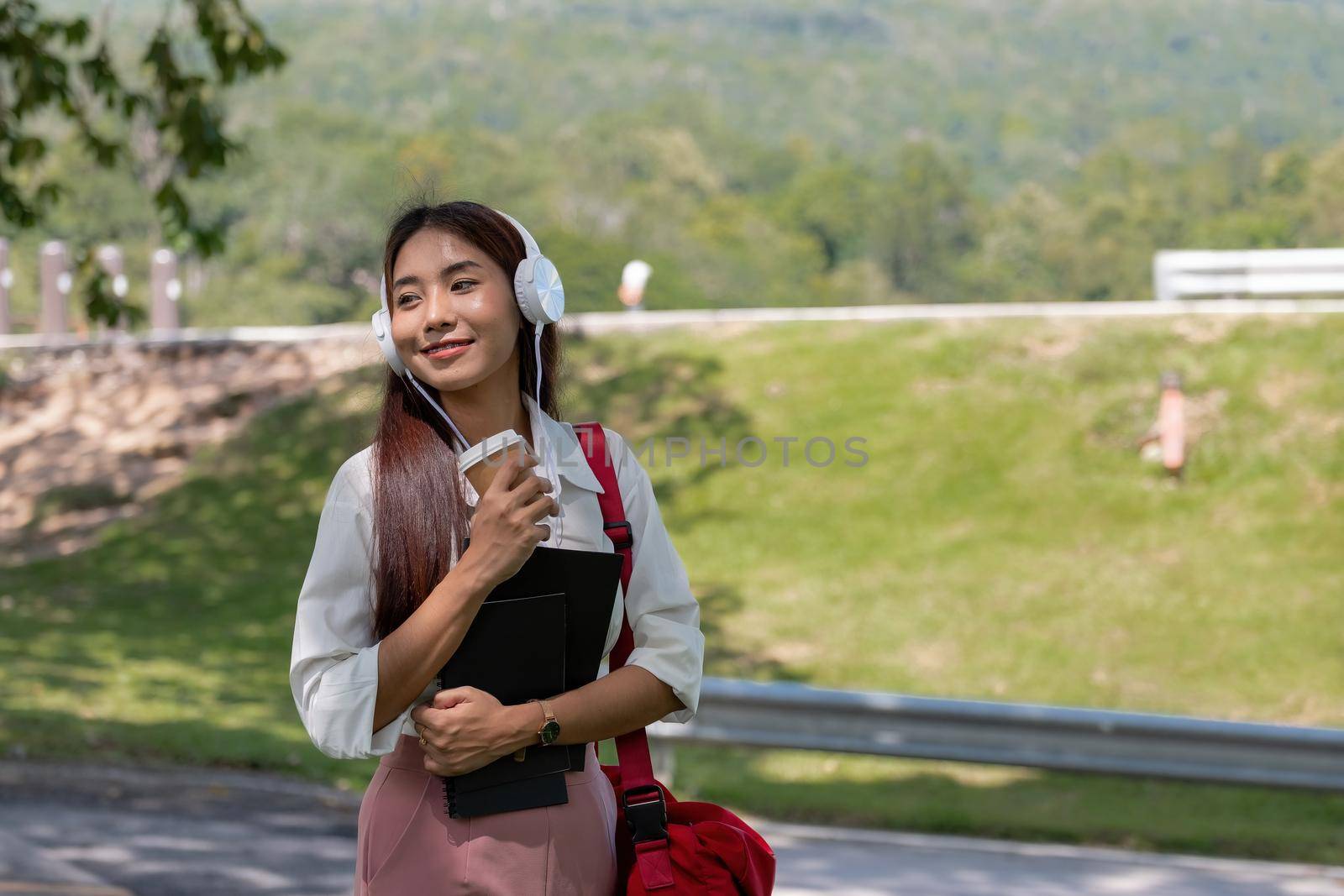 Happy young beautiful asian woman wearing headset and holding notebook in park