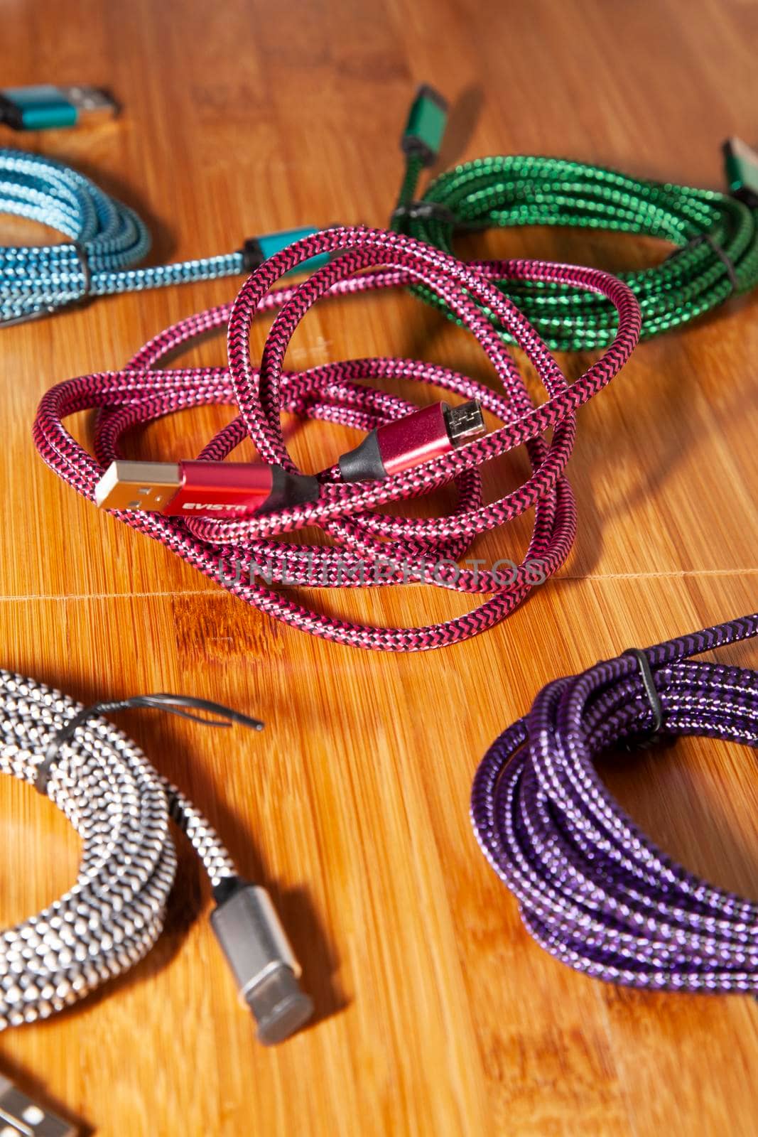 Pink charging cord in the middle of green, blue, purple, and silver charging cords on a wooden table